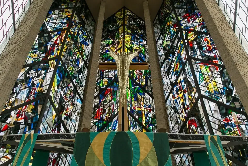Large stained glass windows and a crucifix inside the church reflect the rich history of the chapel, viewed from the altar area.