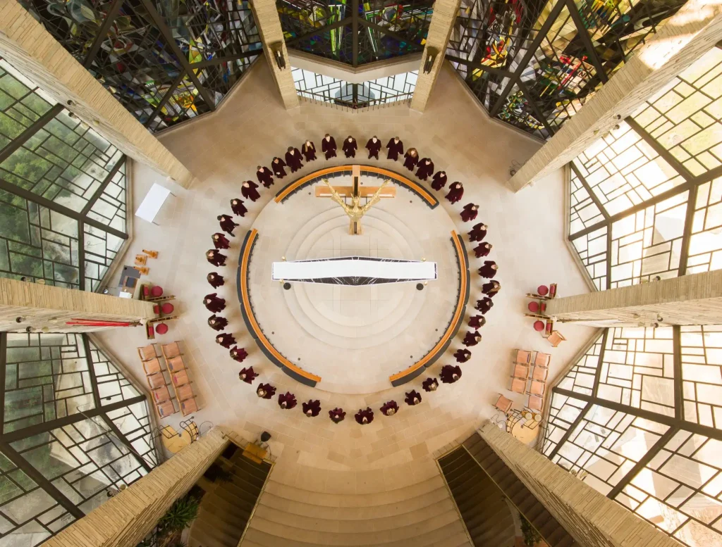 Aerial view of people in robes forming a circle around a central altar in a modern, stained-glass chapel, echoing the rich history of the chapel.