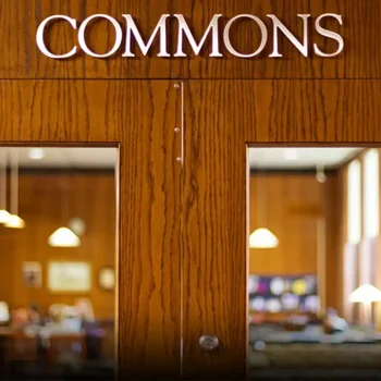 Wooden doors with "COMMONS" written above, showing a warmly lit room with tables and hanging lights inside.