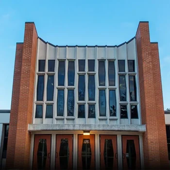 A brick building with tall, narrow windows and four glass doors under a clear blue sky.