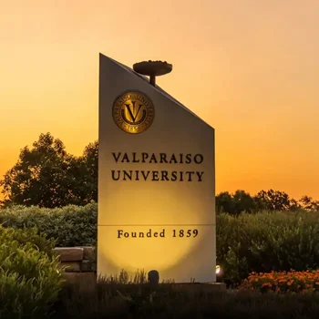 Valparaiso University sign at sunset, with trees and flowers in the background, and "Founded 1859" inscribed.