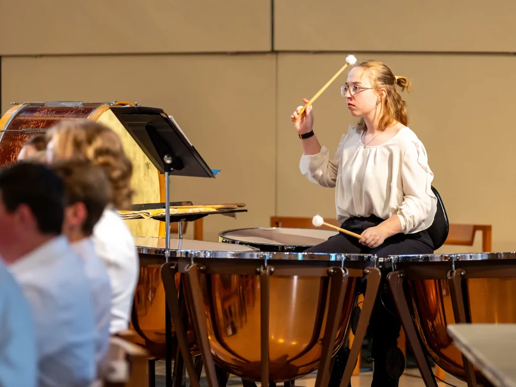 A woman plays timpani drums with mallets during a musical performance in the Chapel of the Resurrection concert hall.