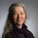 Smiling woman with long gray hair, identified as Laurie Eberhardt, Ph.D., wearing a purple scarf and dark top against a gray background.