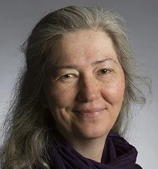 Laurie S. Eberhardt, a middle-aged woman with long gray hair, smiles softly at the camera while wearing a dark scarf.
