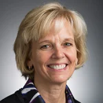 Smiling middle-aged woman, Julie Peller, with short blonde hair, wearing a patterned scarf and hoop earrings.