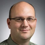 Smiling man, Kevin L. Jantzi, with glasses and a collared shirt against a gradient gray background.