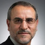 A middle-aged man with glasses, a beard, and short hair, wearing a suit, poses against a gray background. This professional is Zuhdi Aljobeh, Ph.D., P.E.
