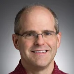 A middle-aged man with glasses, short hair, and a maroon collared shirt, Peter Weiss, Ph.D., P.E., is smiling at the camera.