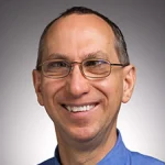 Smiling man with glasses wearing a blue shirt, identified as Bart Wolf, Ph.D., photographed in front of a plain, gradient background.