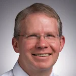 Smiling man with glasses, short light brown hair, wearing a white shirt, facing forward—Craig Clark, Ph.D.