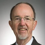 Donald Koetke, an older man with glasses, short hair, and a goatee, is seen wearing a suit and smiling at the camera.