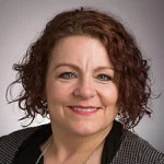 Smiling woman with curly brown hair, Sonja Streuber, wearing a patterned jacket and necklace against a plain background.