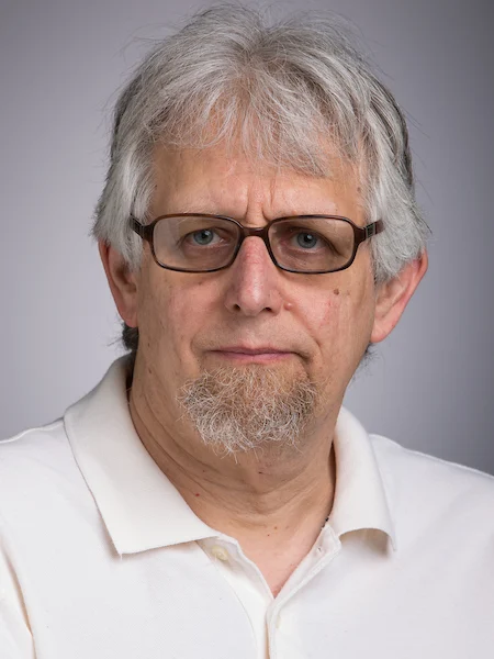 Older man with gray hair, glasses, a short beard, and a white polo shirt facing the camera—could be Michael Glass.