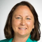 Smiling woman, Julie Brandy, with shoulder-length brown hair wearing a teal blazer against a plain background.