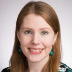 Smiling woman with long light brown hair, turquoise earrings, and a light patterned top on a plain background; Tiffany Kolba.