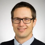 Smiling man with short brown hair, glasses, and wearing a collared shirt and sweater—Christopher Iceman, Ph.D.