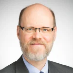 A middle-aged man with glasses, a beard, and a suit, smiling in a professional headshot—perfectly embodying the approachable demeanor of a World Languages professor.