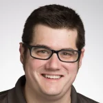 Smiling man with short dark hair and glasses, wearing a dark shirt, against a plain light background—Andrew Butler, Ph.D.