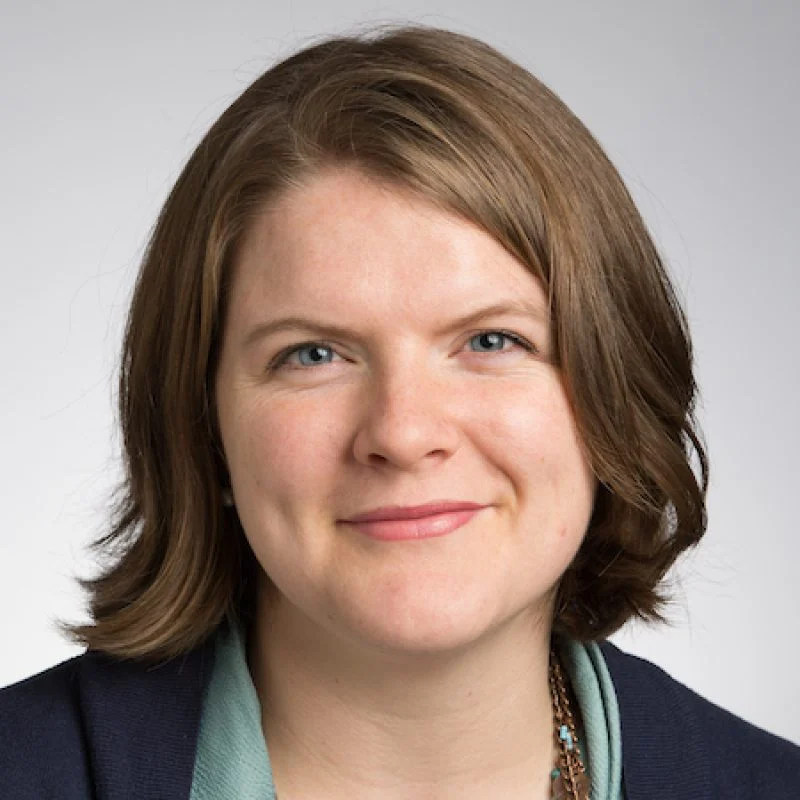 Caroline Ban, a woman with shoulder-length brown hair, smiles at the camera against a plain light background.