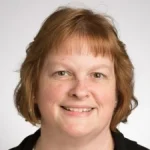 A woman with short, light brown hair smiles at the camera against a plain background.