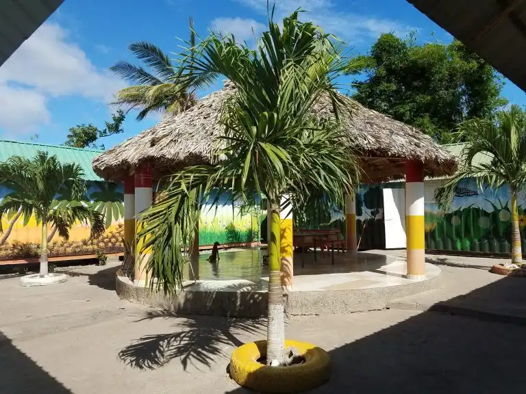 A round thatched-roof gazebo surrounded by palm trees in a sunny courtyard, where you can relax and listen to the distant sound of WAVES.