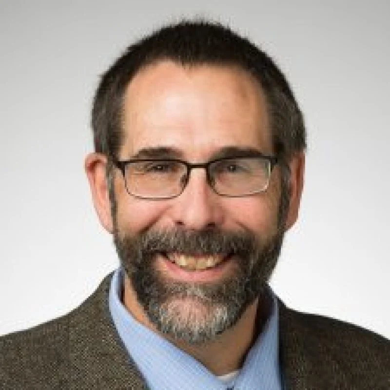Smiling man with glasses, short dark hair, and a beard, wearing a brown jacket and blue shirt. Jay Grossman, P.E., Ph.D., exudes professionalism and warmth.