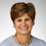 Smiling woman with short brown hair, wearing a light blue top, pearl necklace, and stud earrings—Phrosini Samis-Smith, DHEd, MSSA.