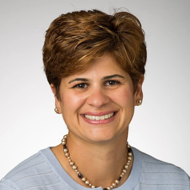 Smiling woman with short brown hair, wearing a light blue top, pearl necklace, and stud earrings—Phrosini Samis-Smith, DHEd, MSSA.