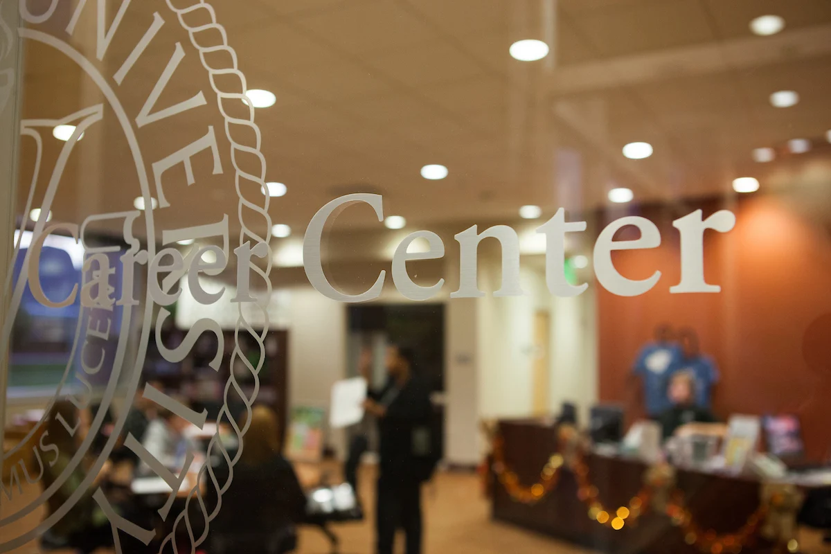 Glass door labeled "Career Center," with people and desks visible in a warmly lit office interior offering valuable student resources.