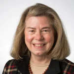 Smiling middle-aged woman with straight, shoulder-length hair, wearing a plaid jacket and beaded necklace—Sarah DeMaris.