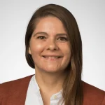 Selina Bartels, with straight brown hair, wearing a white shirt and rust-colored cardigan, smiles at the camera.