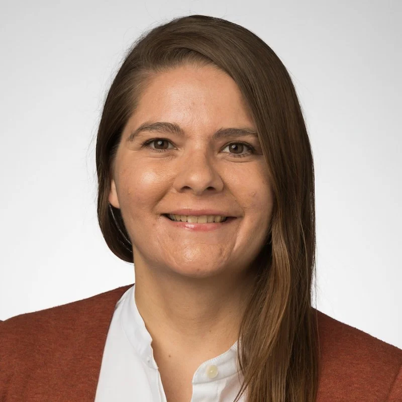 Selina Bartels, with straight brown hair, wearing a white shirt and rust-colored cardigan, smiles at the camera.