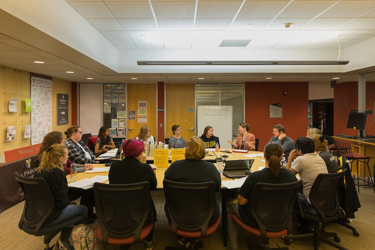 A group of people sit around a table in a meeting room, engaged in discussion about available student resources.