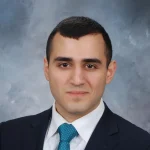 Gor Mkrtchian, dressed in a suit and blue tie, poses for a professional headshot against a gray background.