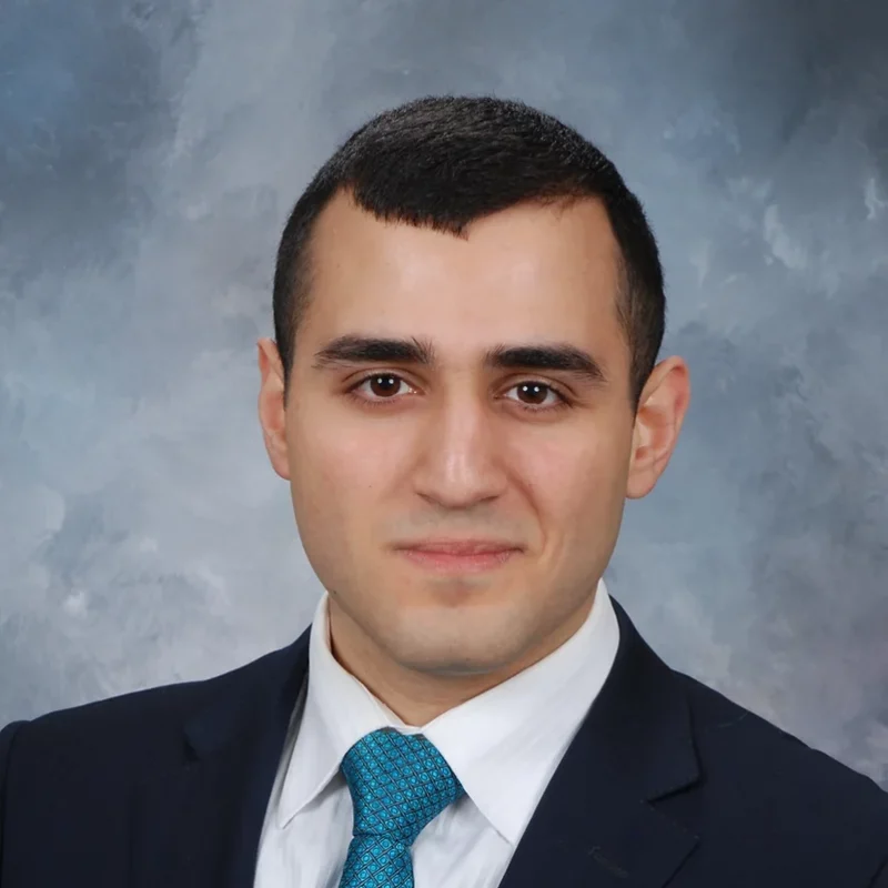 Gor Mkrtchian, dressed in a suit and blue tie, poses for a professional headshot against a gray background.