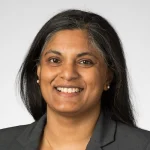 Smiling woman with long dark hair wearing a gray blazer, photographed against a plain light background. Nirupama Devaraj, Ph.D.
