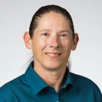 Smiling person with long dark hair in a teal collared shirt against a plain light background, identified as Lisa Driver, Ph.D.
