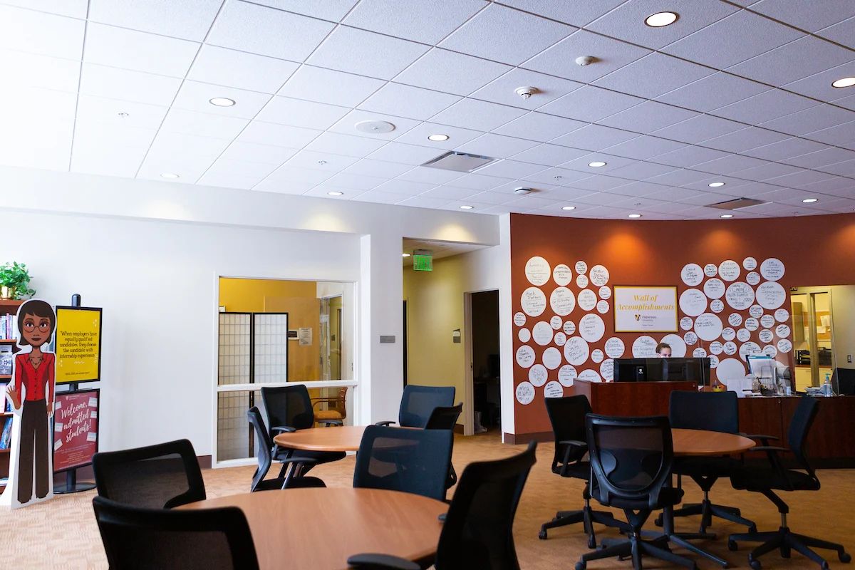 Empty office space with round tables, chairs, and a reception desk in front of a wall with white circles—ideal for organizations seeking workspace funded by grants.
