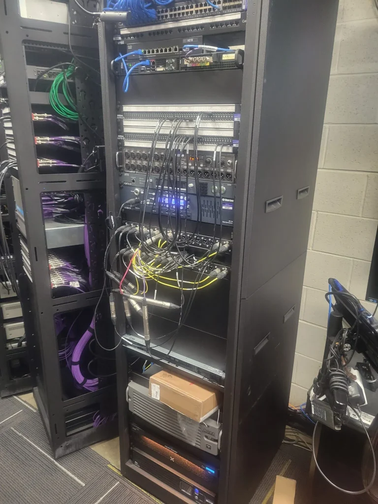 A server rack with various network equipment, cables, and devices organized in a server room for ESPN Valparaiso University Productions.