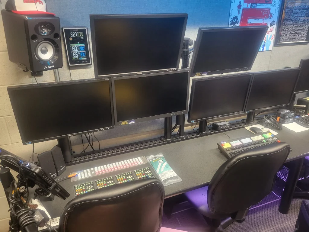 A control room desk with six blank monitors, mixing consoles, speakers, and chairs used by ESPN Valparaiso University Productions.