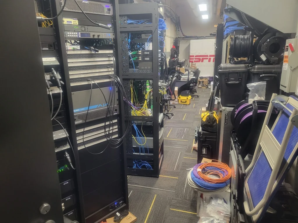 Server racks and equipment fill a cluttered room with cables, cases, and an ESPN Valparaiso University Productions logo visible in the background.