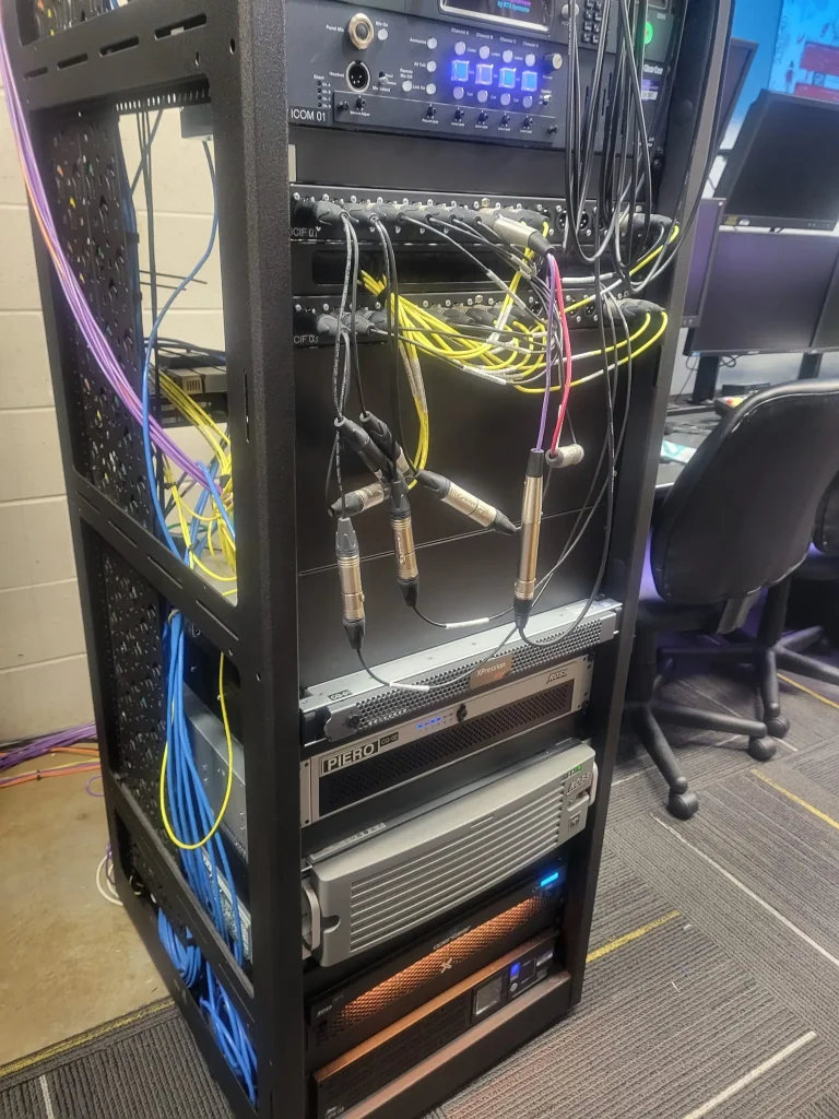 A server rack with various network cables, audio equipment, and electronic devices used by ESPN Valparaiso University Productions in a control room.
