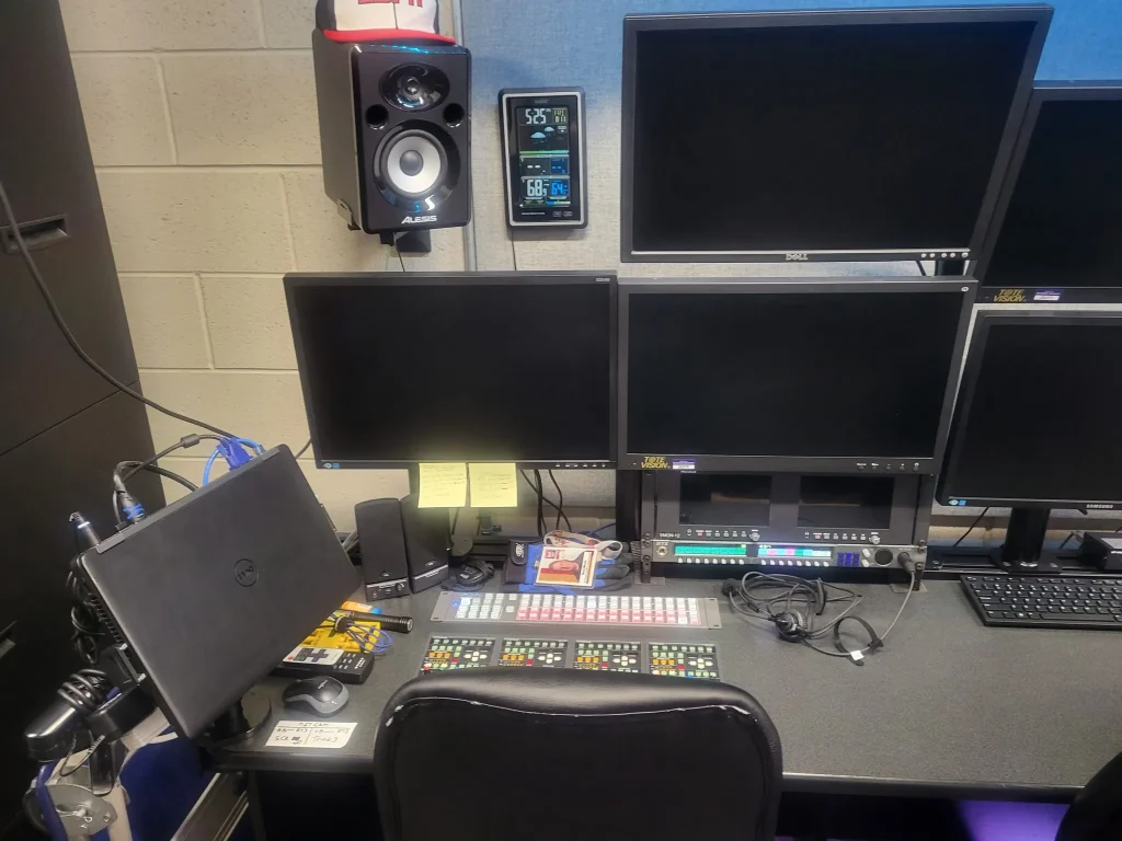 Video editing workstation for ESPN Valparaiso University Productions featuring multiple monitors, control panels, a laptop, and audio equipment on a desk.