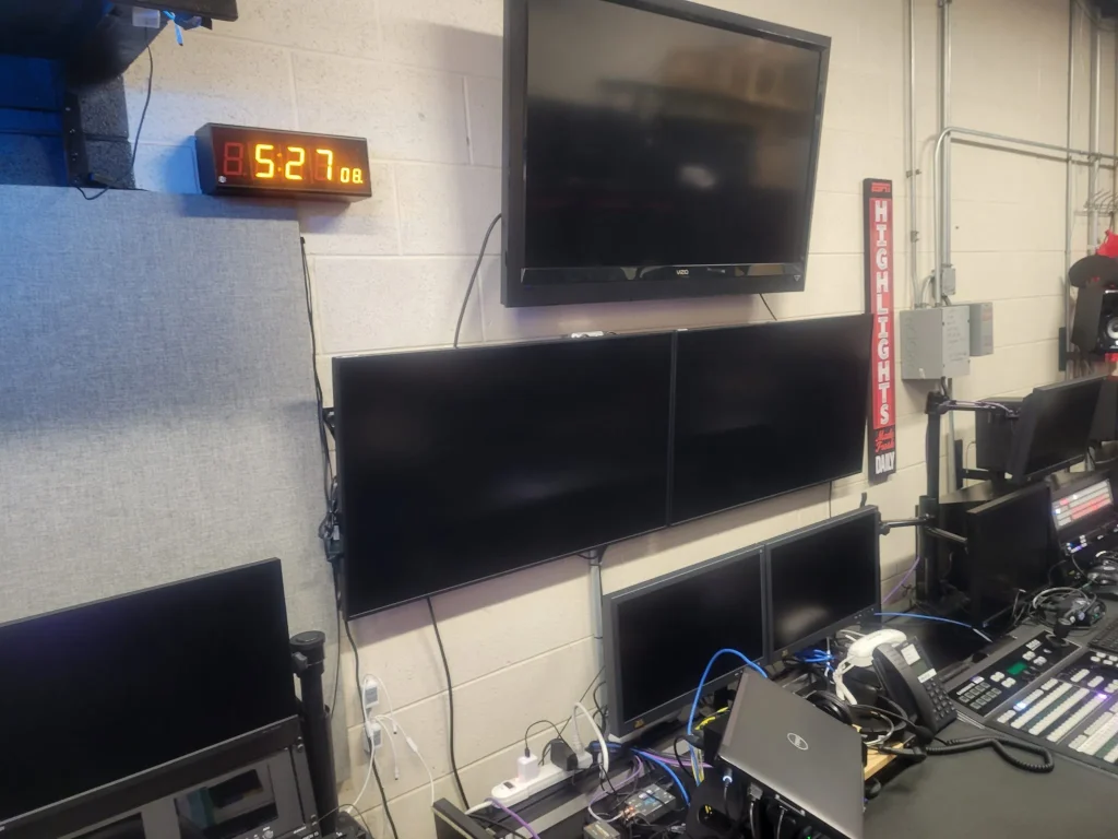 A control room with several blank monitors, a wall clock reading 8:52, and various electronic equipment used by ESPN Valparaiso University Productions.