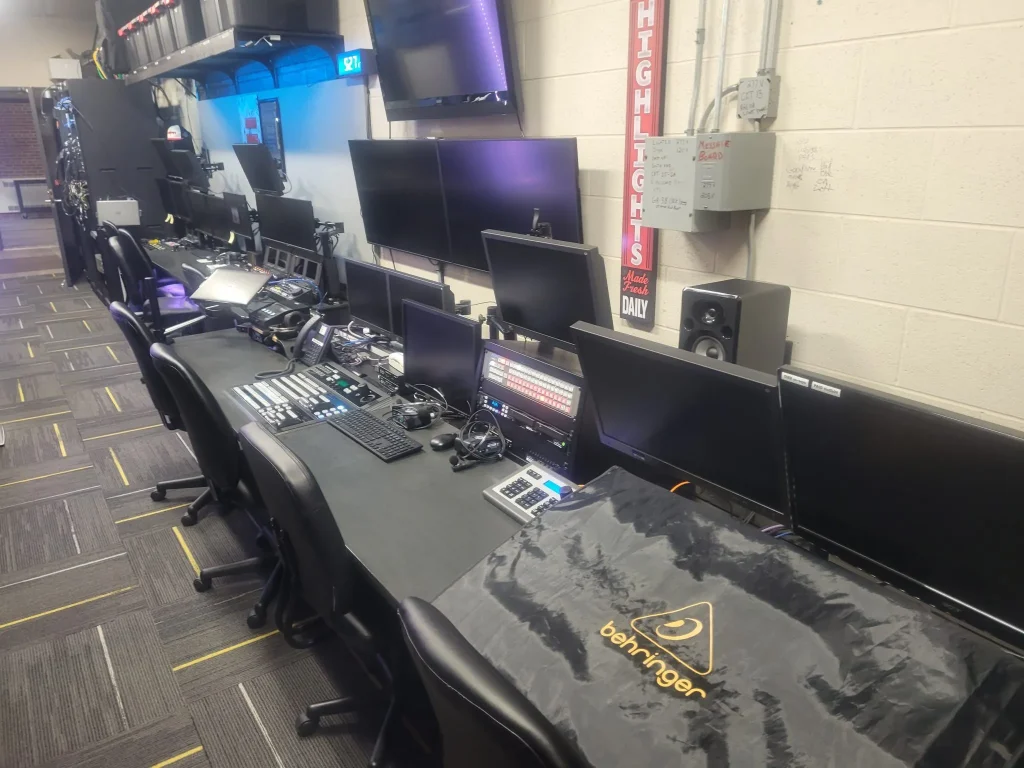 Row of desks with multiple monitors, audio and video equipment, and headsets in an ESPN Valparaiso University Productions control room setup.