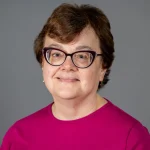 Smiling woman with short brown hair, glasses, and a magenta top against a gray background—Christina Cavinder.
