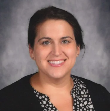 Christine Roberts, a woman with dark hair, smiles while wearing a black and white polka dot blouse and a black sweater.