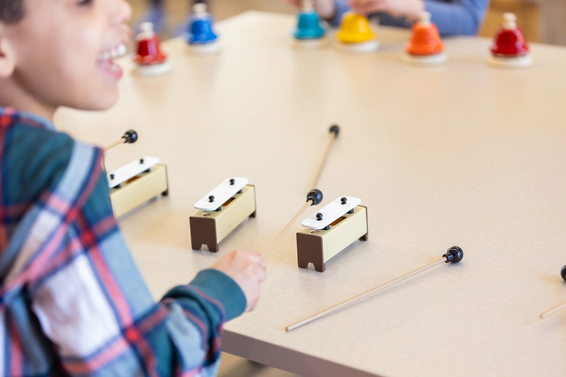 Child engaging in music therapy, playing percussion instruments at a table with colorful handbells in the background.