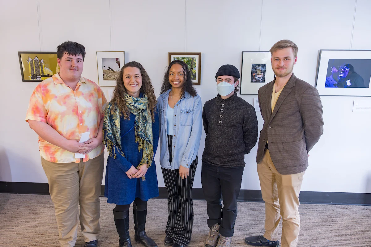 Five people standing indoors in front of a wall with framed artwork, smiling at the camera, proudly representing their services.