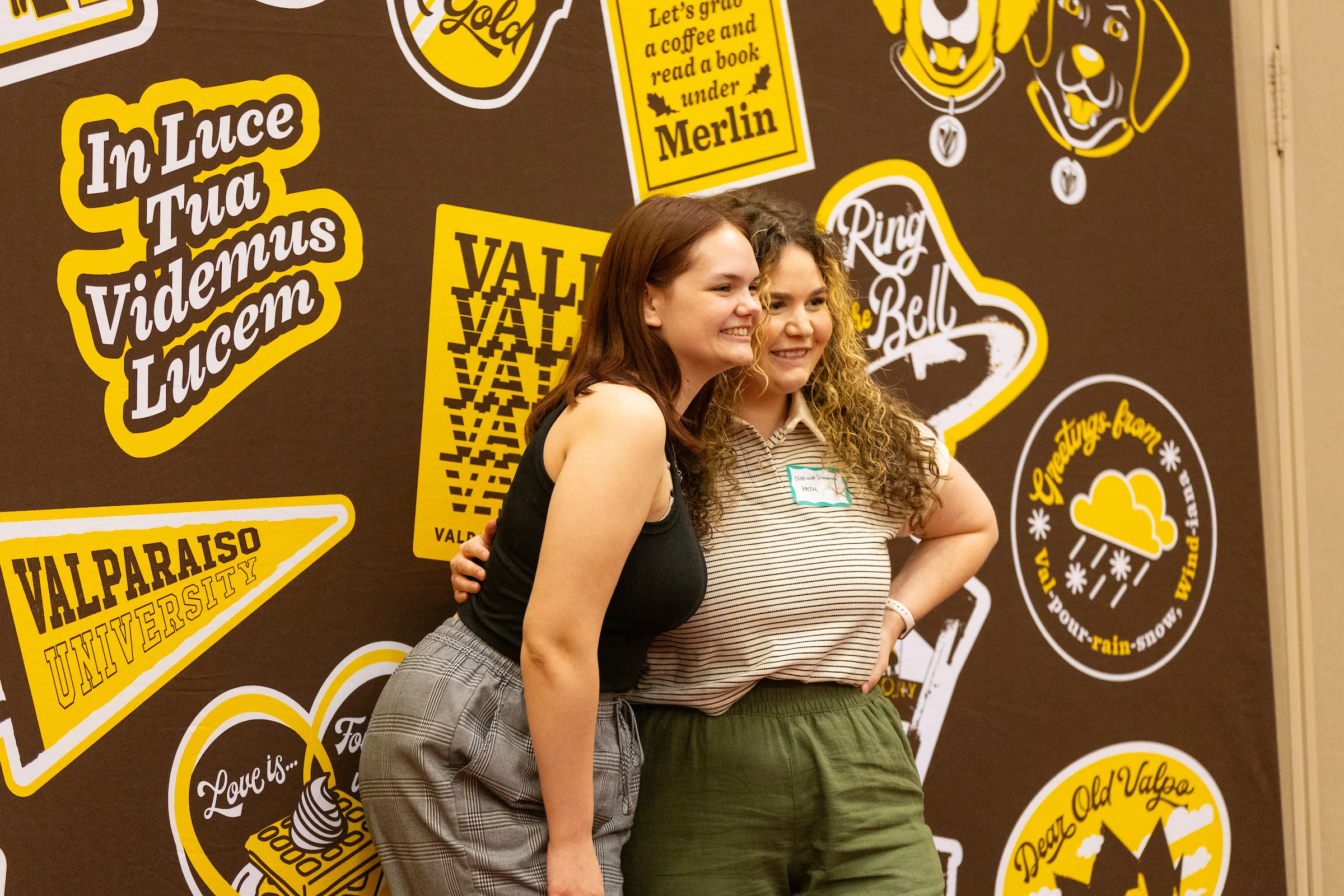 Two women smile and pose together in front of a Valparaiso University themed backdrop with yellow signs, celebrating their achievements in Social Work Foundations.